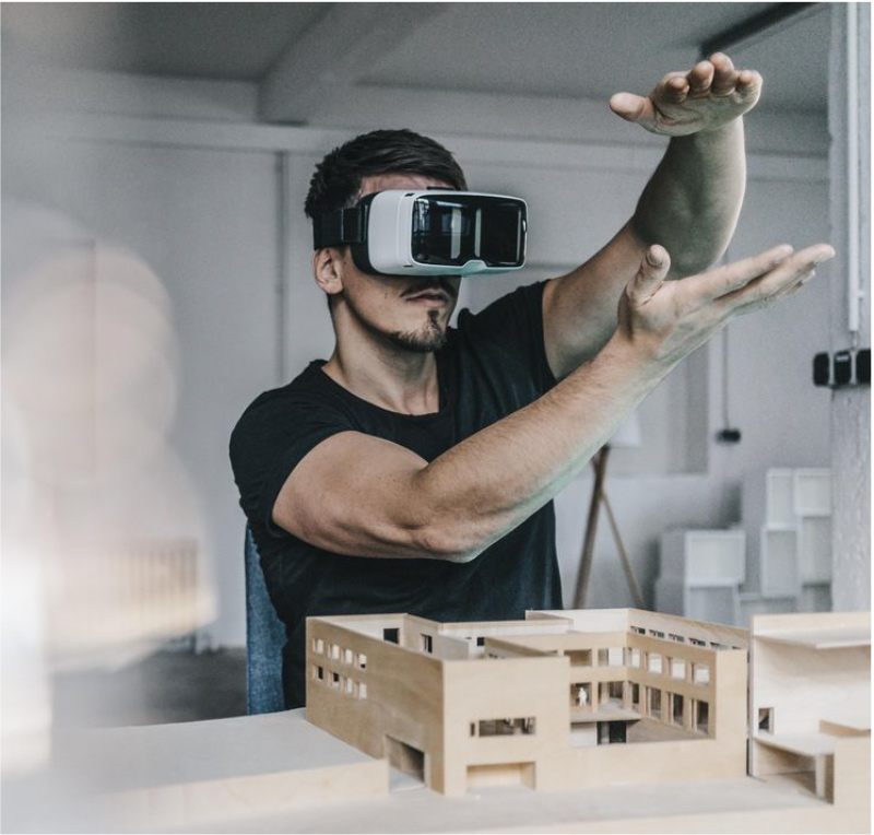 Hombre con unas gafas de realidad virtual que mueve las manos con una maqueta de un edificio frente a él.